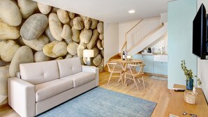 Una sala de estar con sofá, una mesa de comedor con sillas, una zona de cocina y una escalera.