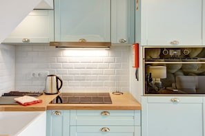 A kitchen with light blue cabinets, a white brick backsplash, a stainless steel kettle, and a digital oven clock.