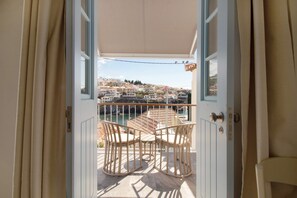 Une porte ouverte donnant sur un balcon agrémenté de fauteuils en osier et offrant une vue sur une ville côtière.
