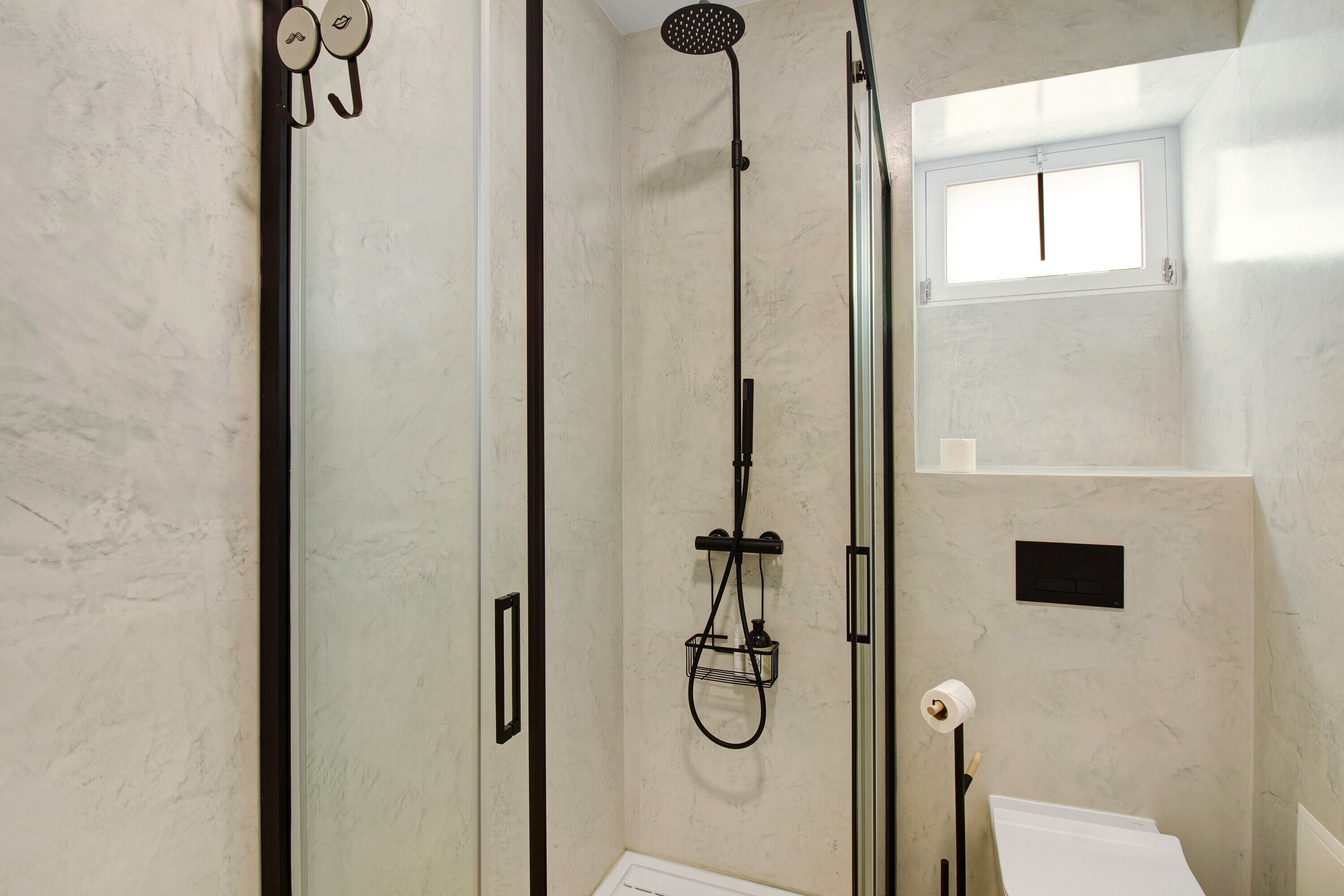 Een douche met een handdouche, een wandmengkraan en een klein raam boven de douche.