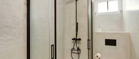 Een douche met een handdouche, een wandmengkraan en een klein raam boven de douche.