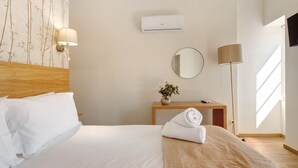 Habitación de hotel con cama, lámpara de noche, una mesita con un florero y aire acondicionado de pared.