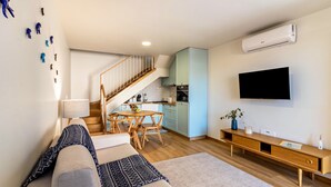 A modern living room with a sofa, a wooden dining table, and a kitchen area with cabinets and a TV. - Holiday Home "Casa das Andorinhas" with Private Terrace & Wi-Fi (Câmara de Lobos)