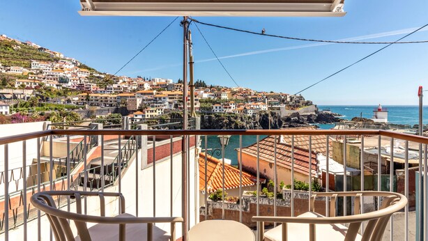 A balcony with a view of a coastal town, including buildings and a lighthouse. - Holiday Home "Casa das Andorinhas" with Private Terrace & Wi-Fi (Câmara de Lobos)