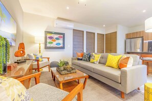 A modern living room with a sofa, coffee table, and chairs. There is a painting on the wall and a plant on the side table.