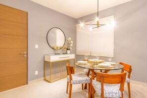 A dining area with a round glass table, wooden chairs, a white console table with a mirror, and a pendant light. - Ocean-View Condo, 9 Pools & Turtle Beach (Akumal)