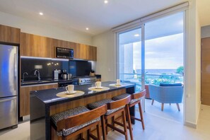 A modern kitchen with a central island, stainless steel appliances, and a large sliding glass door leading to a balcony with a view.