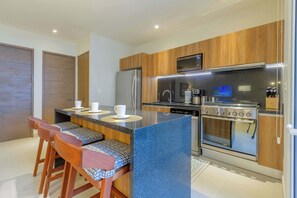 A modern kitchen with a central island, bar stools, a built-in oven, and a microwave. - Ocean-View Condo, 9 Pools & Turtle Beach (Akumal)