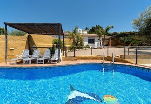 A swimming pool with lounge chairs and a covered area, surrounded by a building and vegetation. - Holiday Home Los Aperos 1 with Sea View, Pool, Garden & Wi-Fi (Vélez-Malaga)