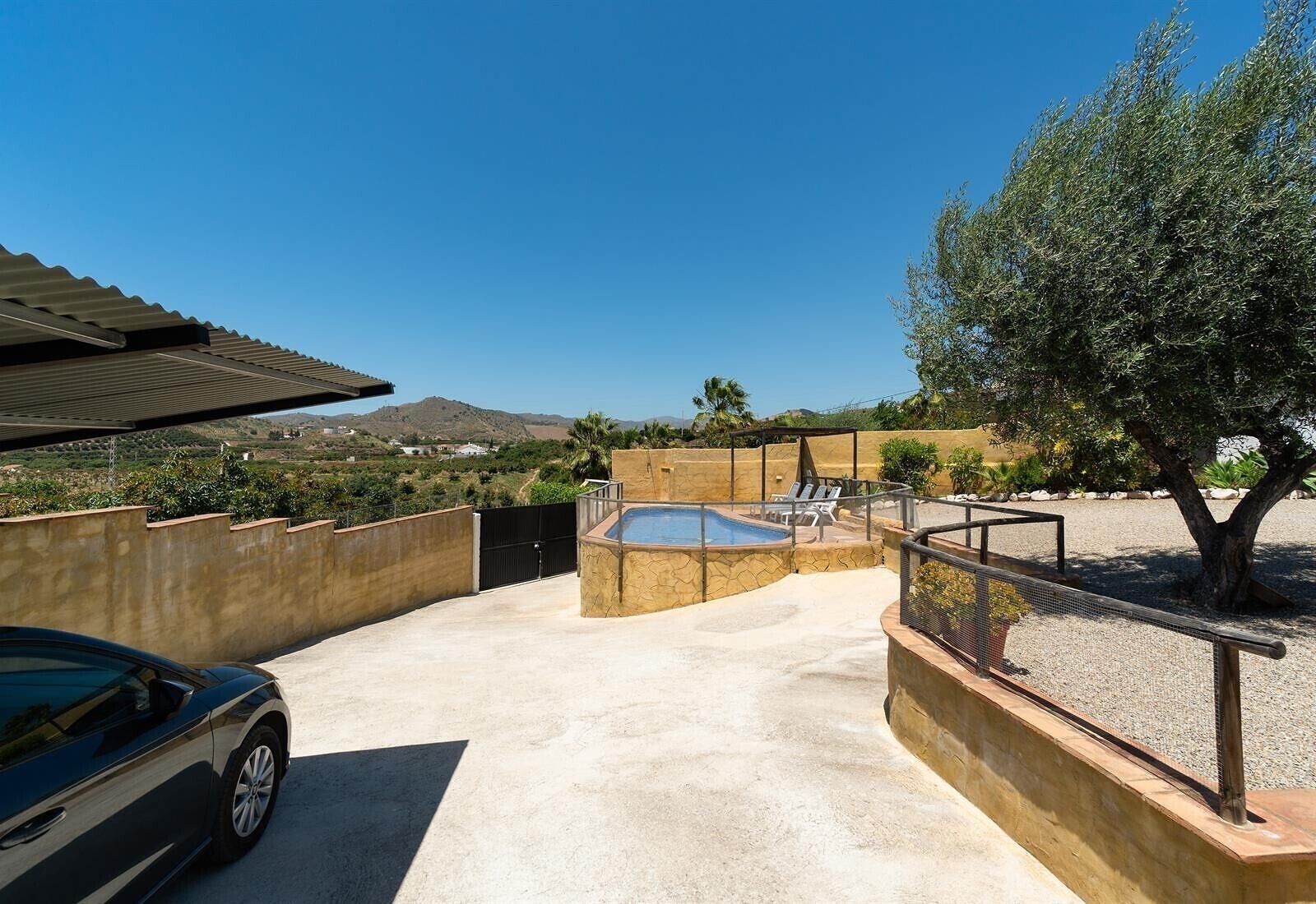 Une piscine entourée de pierres, une voiture et un arbre dans un espace extérieur ensoleillé.