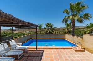 Une piscine avec vue sur la campagne, entourée de palmiers et agrémentée d’une pergola.