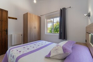 Une chambre à coucher avec un lit, une armoire en bois, une fenêtre avec des rideaux et un radiateur.