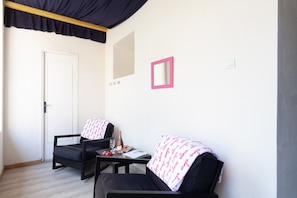 Une pièce avec deux chaises noires, une petite table sur laquelle se trouvent une bouteille de vin, des verres et un carnet. Il y a une porte blanche et un miroir au mur.