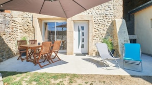 A stone building with a patio, a table with chairs, a blue lounge chair, and a large umbrella. - Holiday Home 'La Mottinière' with Private Terrace and Wi-Fi (Saint-Hilaire-du-Rosier)