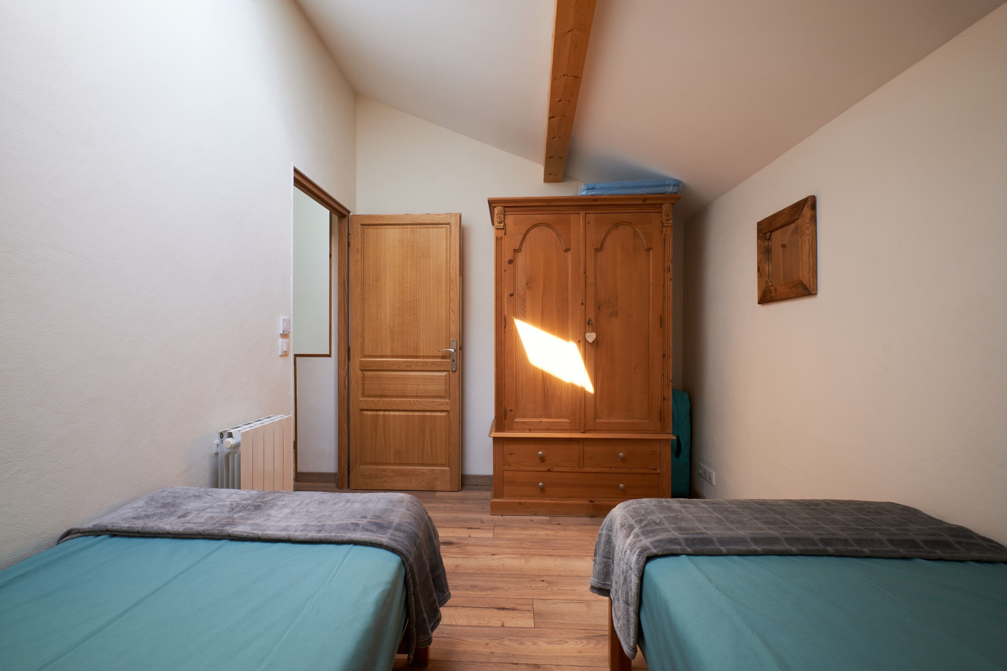A bedroom with two beds, a wooden wardrobe, and a door leading to another room.