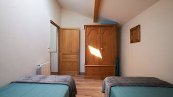 A bedroom with two beds, a wooden wardrobe, and a door leading to another room.