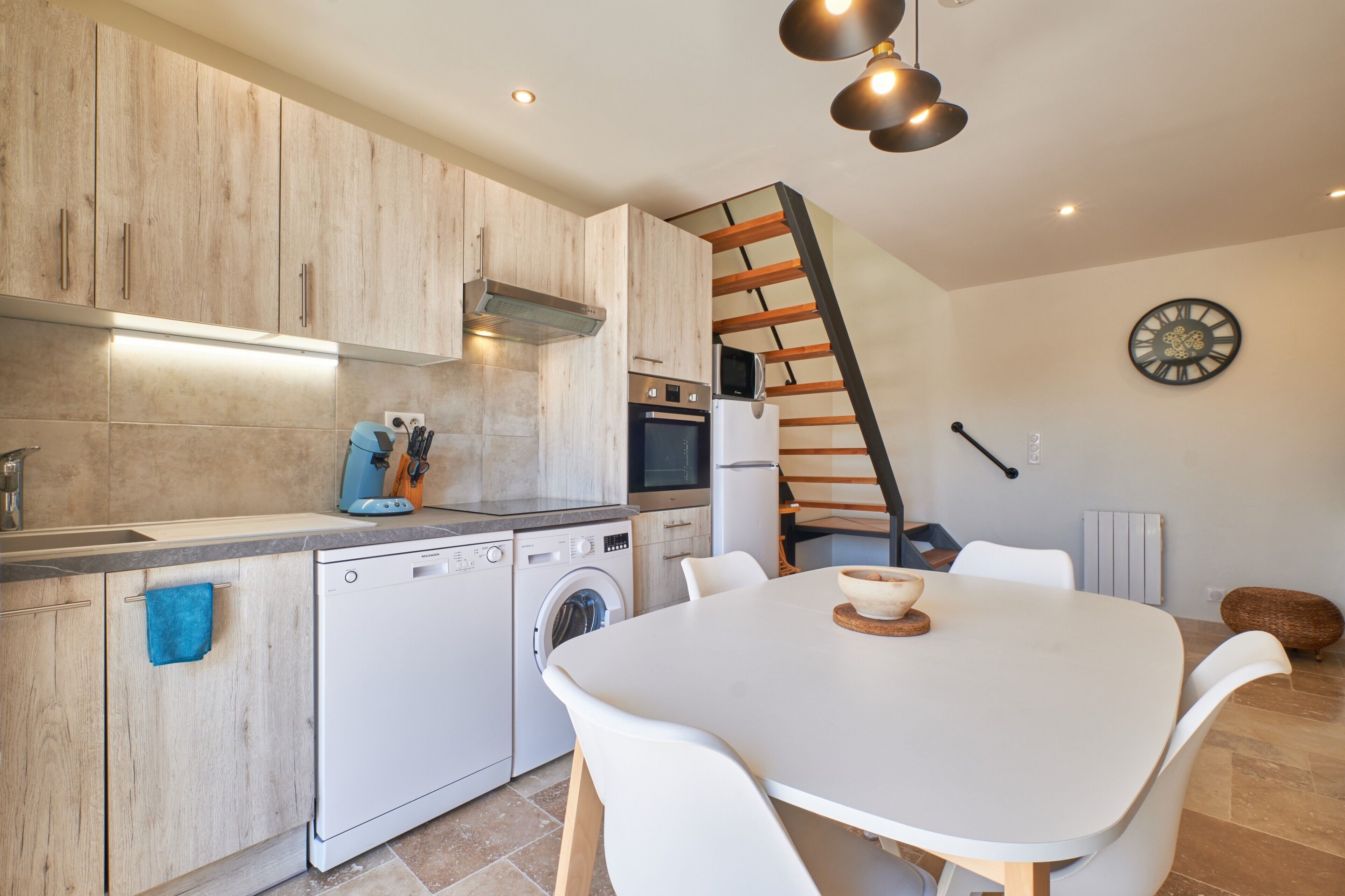 Une cuisine moderne avec des meubles en bois, un lave-vaisselle, un lave-linge et un coin repas comprenant une table et des chaises.