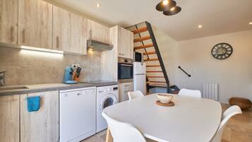 Une cuisine moderne avec des meubles en bois, un lave-vaisselle, un lave-linge et un coin repas comprenant une table et des chaises.