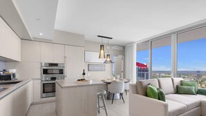 A modern kitchen with built-in appliances, a dining area with a table and chairs, and a large window offering a city view.