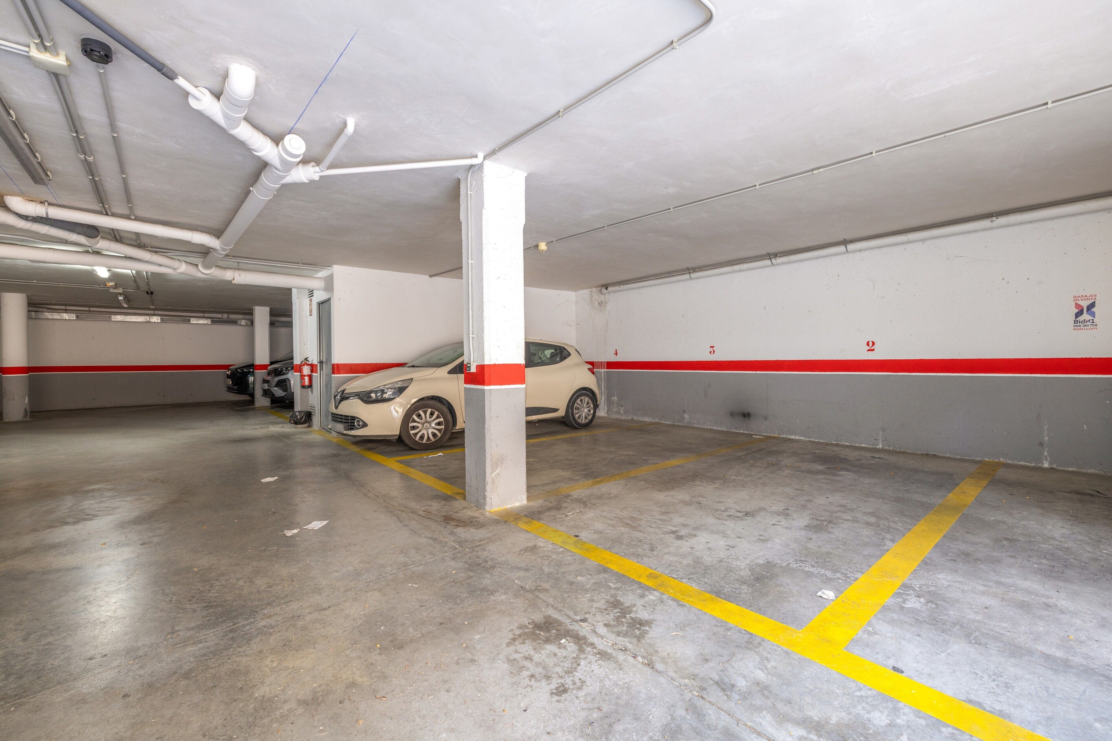 Eine Parkgarage mit Betonböden, weißen Wänden und roten Streifen.