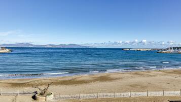 A beach with a fence, a rocky outcrop, and mountains in the distance.