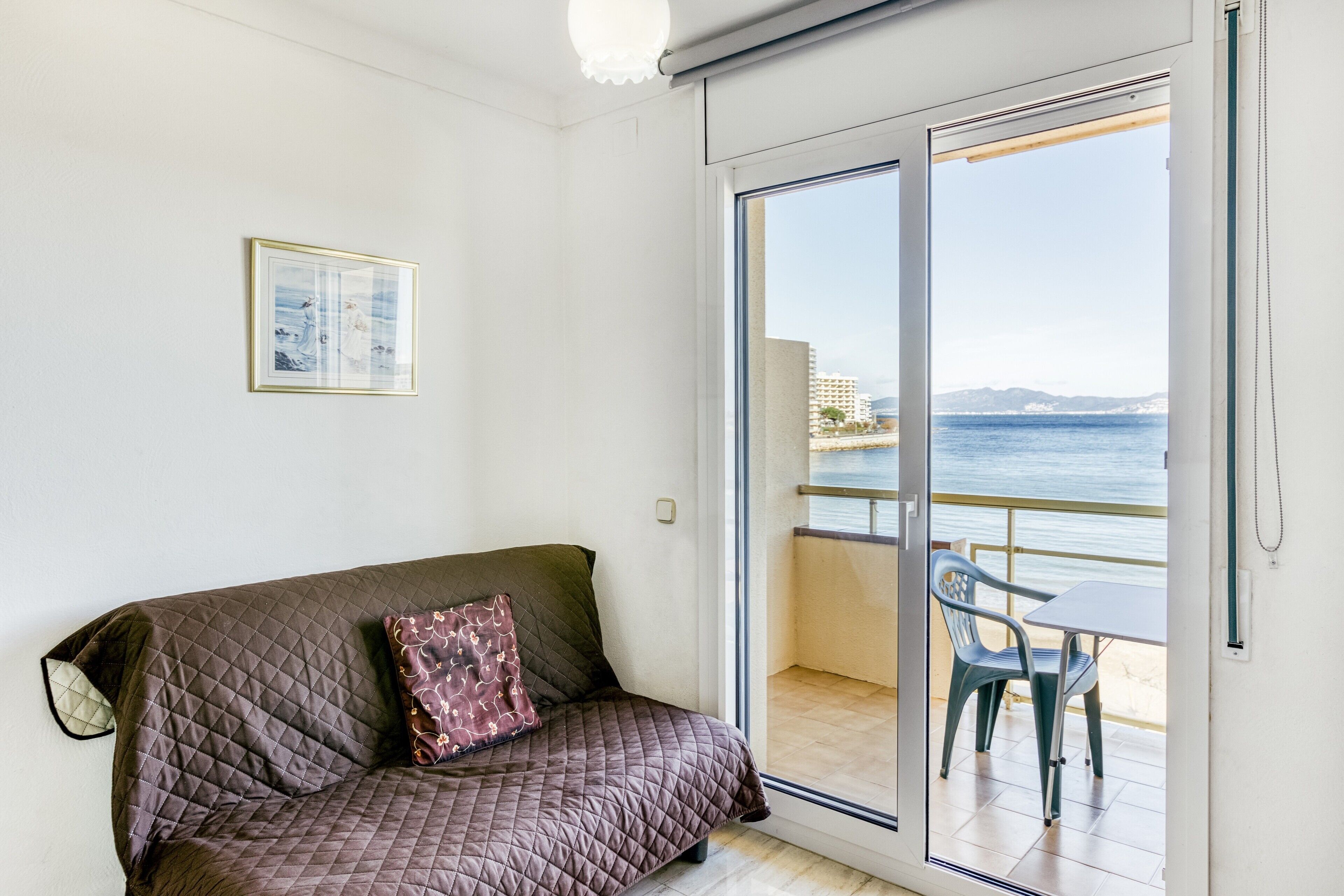 Una habitació amb un llit, un quadre al mur i un balcó amb vistes al mar.