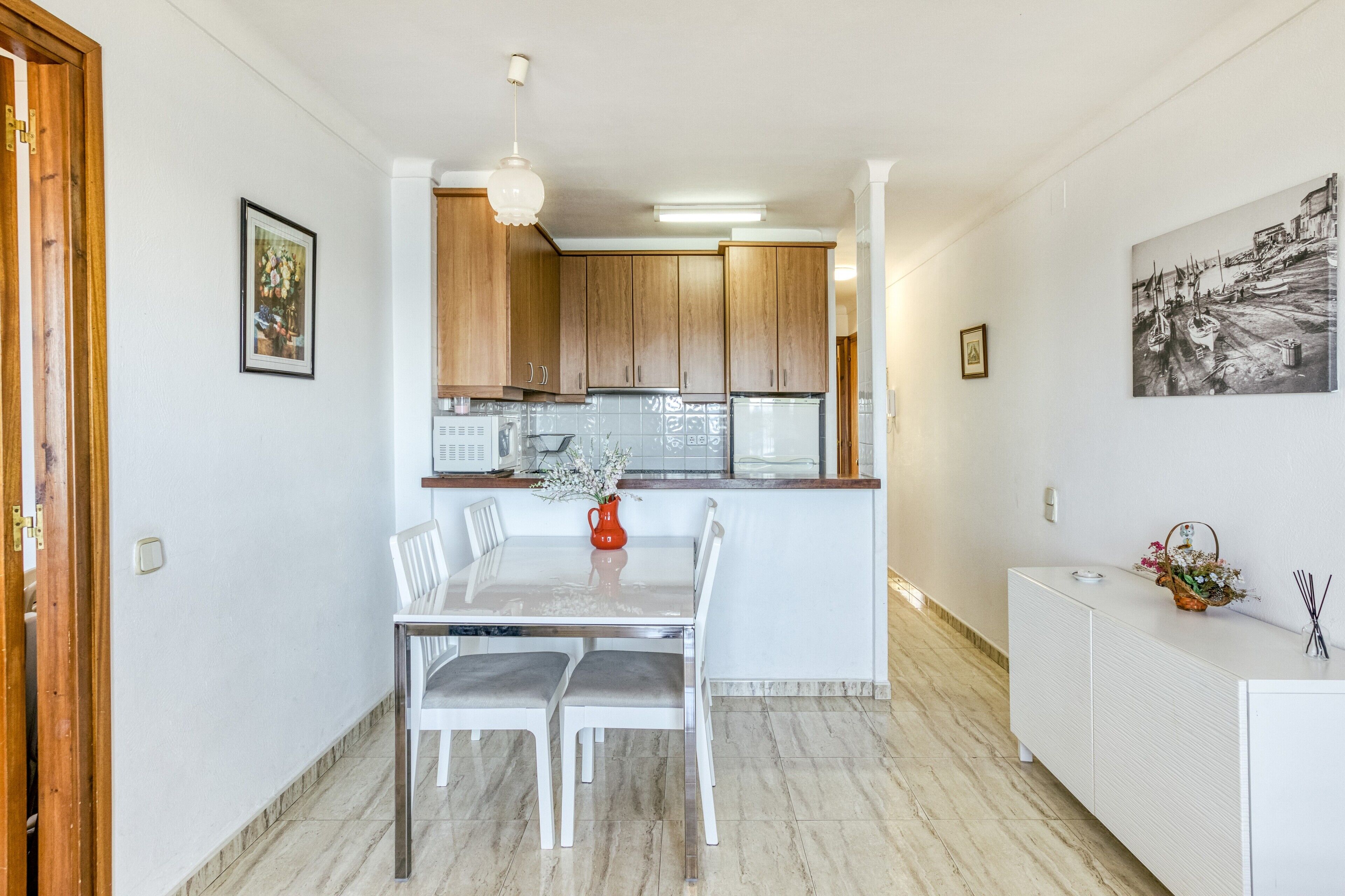 Een moderne keuken met houten kasten, een witte eettafel met stoelen en een keukeneiland.