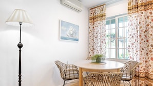 Un coin repas avec une table ronde, des chaises en osier, un lampadaire, un tableau et des rideaux à motifs floraux.