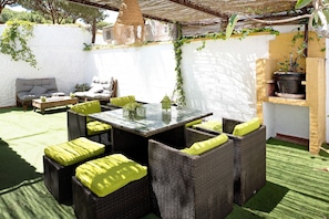 A patio area with wicker furniture, a glass-top table, and a potted plant. - Villa "Percebes" with Private Pool, Private Terrace & Wi-Fi (Chiclana de la Frontera)