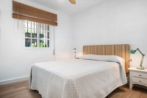 A bedroom with a bed, a nightstand, a lamp, a window with blinds, and a wall-mounted light switch. - Villa "Percebes" with Private Pool, Private Terrace & Wi-Fi (Chiclana de la Frontera)