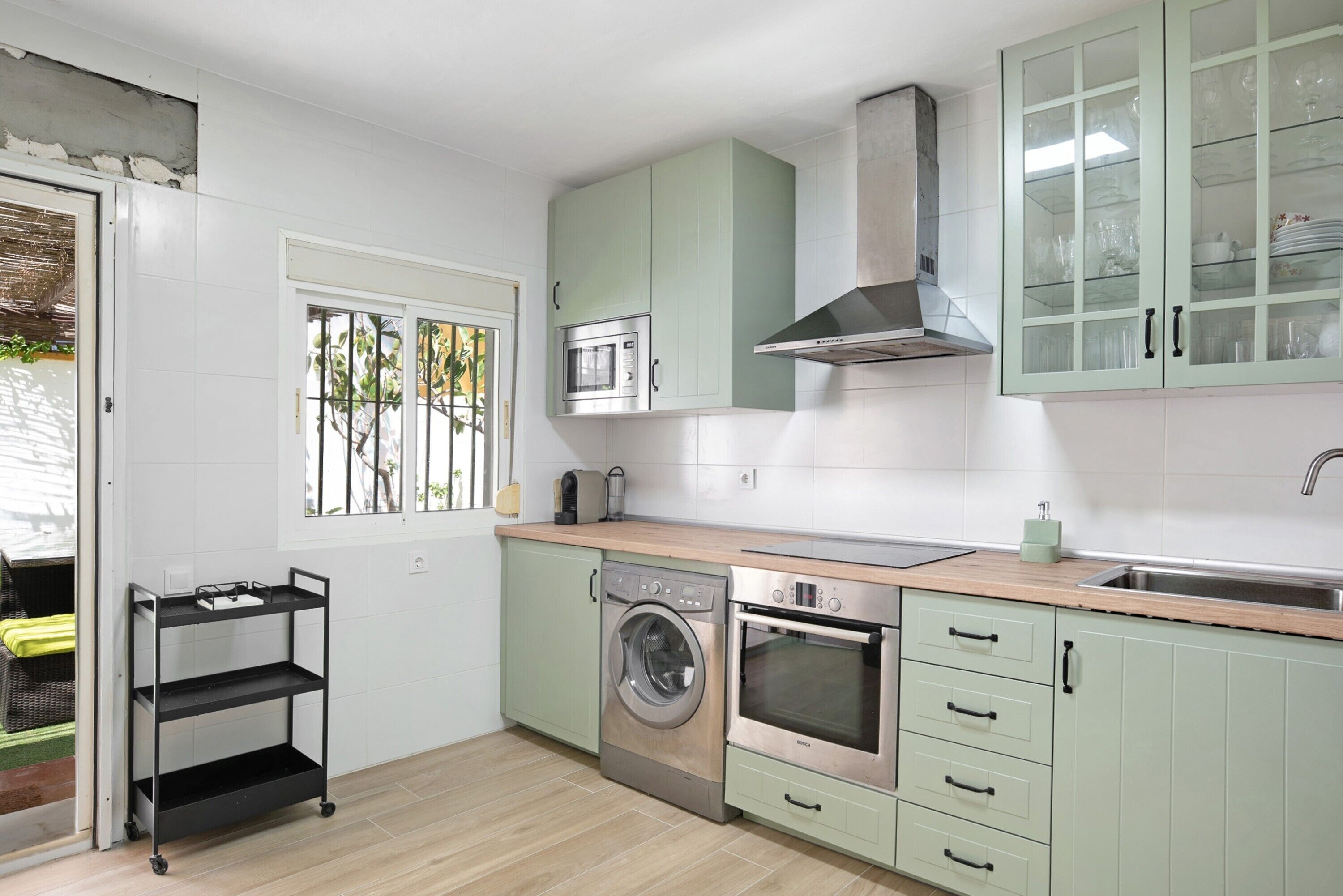A compact kitchen with a washing machine, oven, microwave, and a cabinet with glass doors.