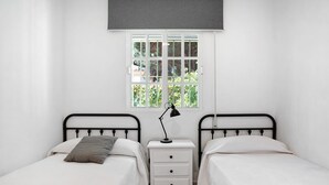 Une chambre double avec deux lits, une table de chevet, une lampe et une fenêtre donnant sur un paysage verdoyant.