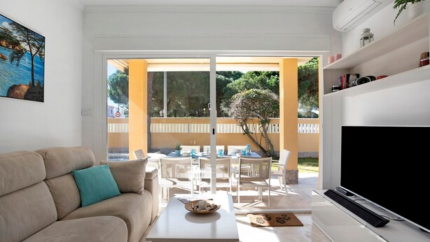 Een woonkamer met een bank, een salontafel, een televisie en een balkon met buitenmeubilair.
