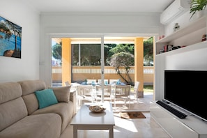 A living room with a sofa, a coffee table, a TV, and a balcony with outdoor furniture.