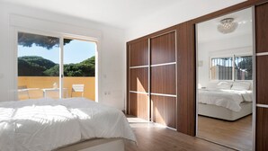 Een slaapkamer met een groot bed, een inloopkast met schuifdeuren en uitzicht op groen.