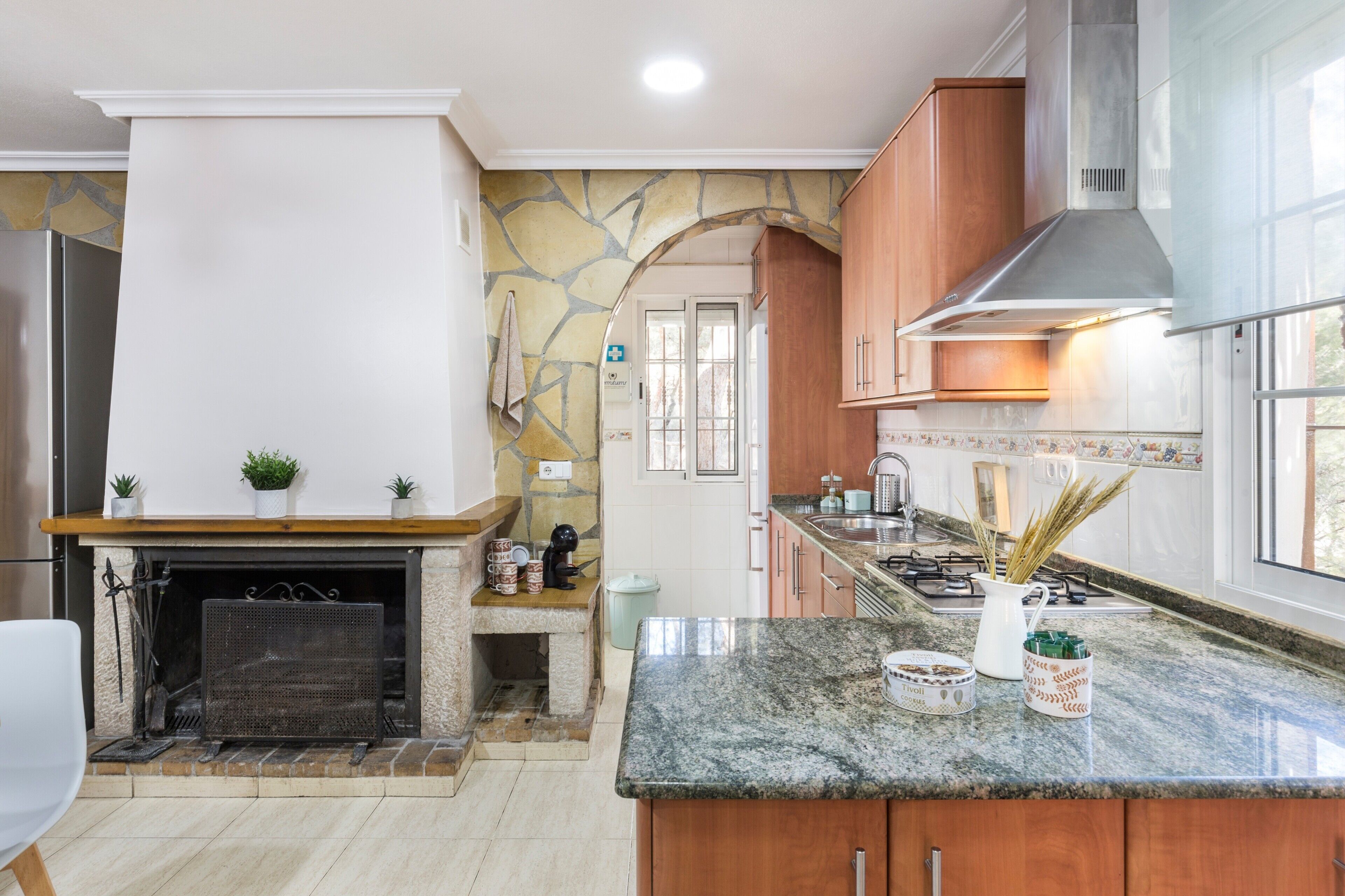 Een moderne keuken met een stenen openhaard, granieten aanrechtbladen, houten kastjes en uitzicht op het omliggende landschap.