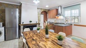 A modern kitchen with a wooden dining table, stainless steel appliances, and a stone accent wall.