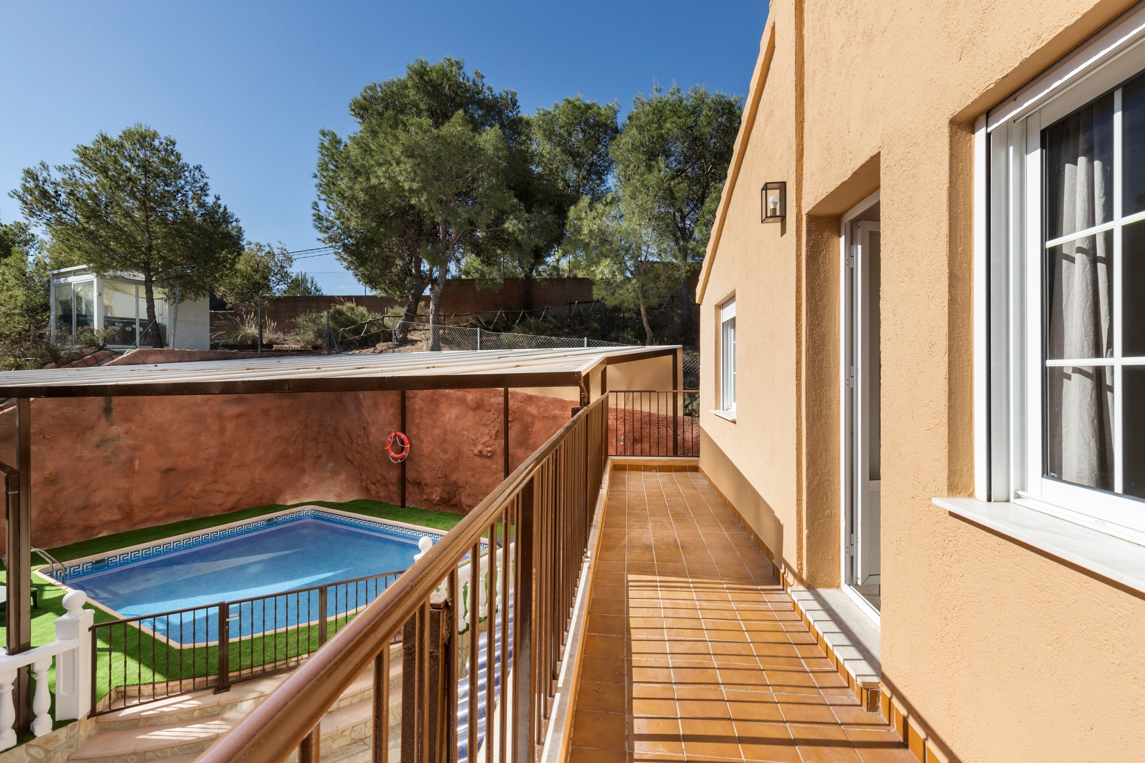 A residential property with a swimming pool, a balcony with a railing, and a view of trees and a clear sky.