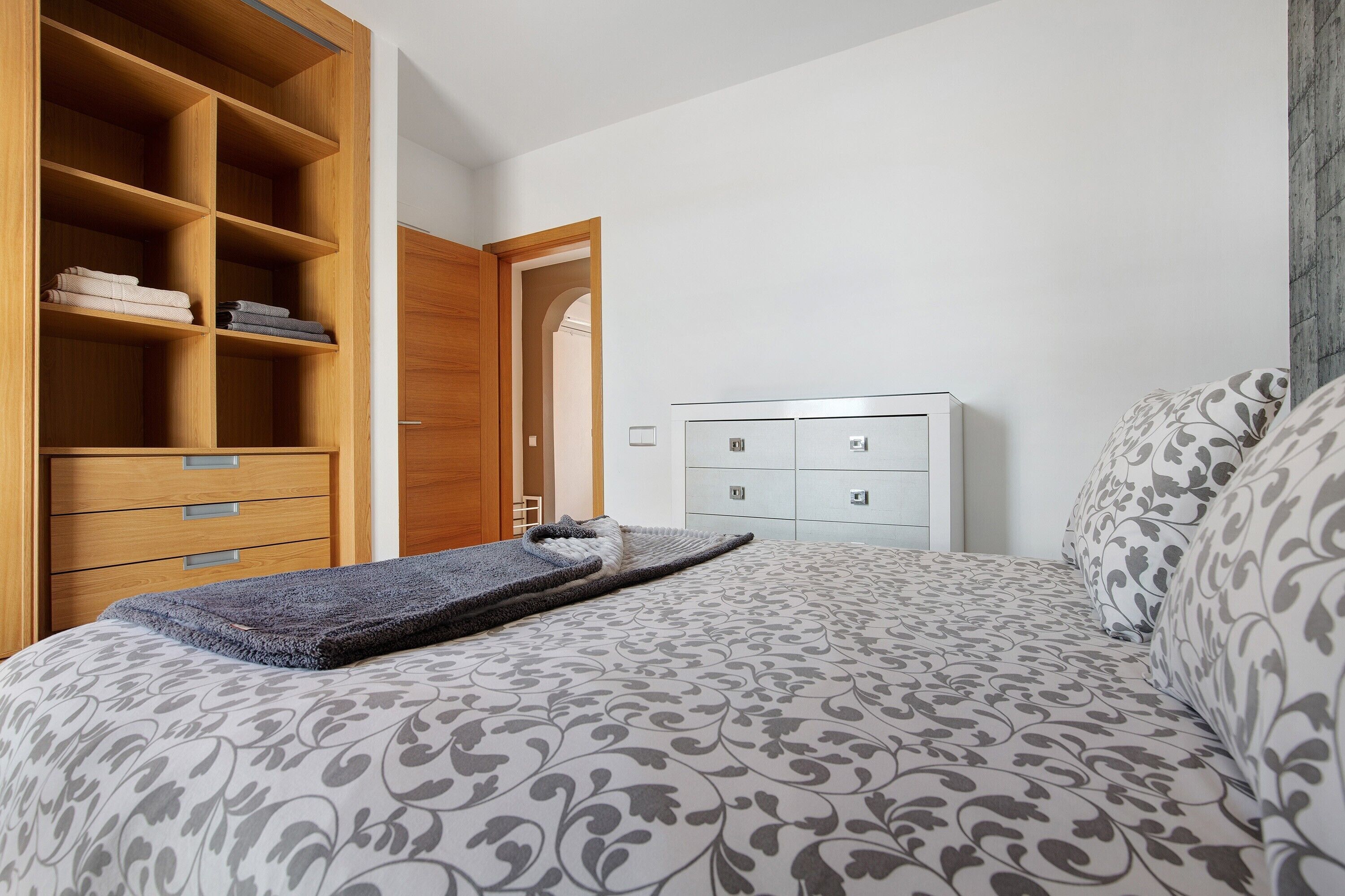 Un dormitorio con una cama, un armario de madera, un tocador y una puerta que da a otra habitación.