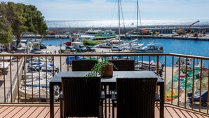 A balcony with wicker furniture and a potted plant, overlooking a marina with boats and a clear sky. - Holiday Apartment 'Es Port' close to the Beach with Sea View, Terrace & Wi-Fi (Cala Rajada)