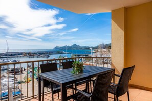 Een balkon met een tafel en stoelen, uitkijkend op een jachthaven met boten en een bergachtig landschap.