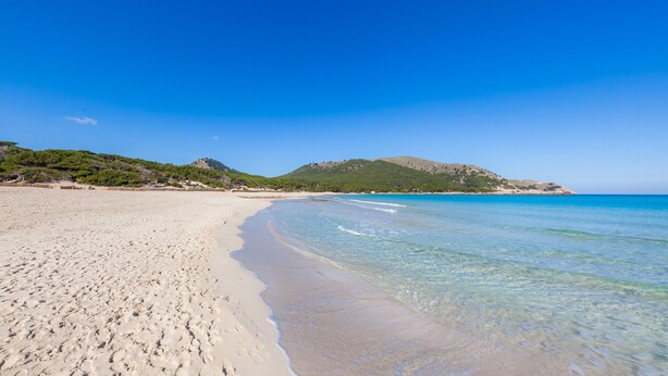 A beach with clear water, sandy shore, and a hill in the background. - Holiday Apartment 'Es Port' close to the Beach with Sea View, Terrace & Wi-Fi (Cala Rajada)