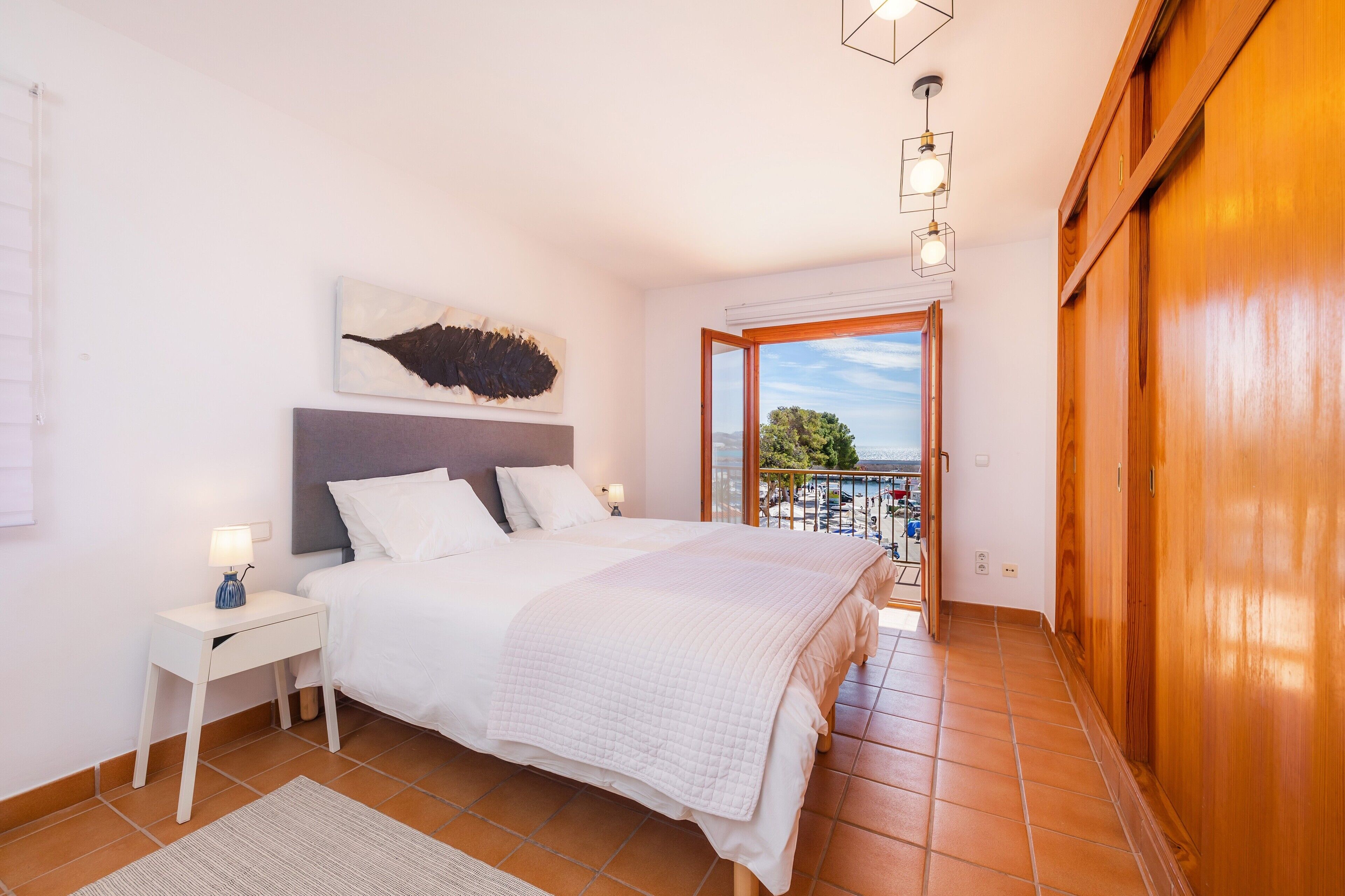 Quarto com cama, mesa de cabeceira e vista para o exterior.