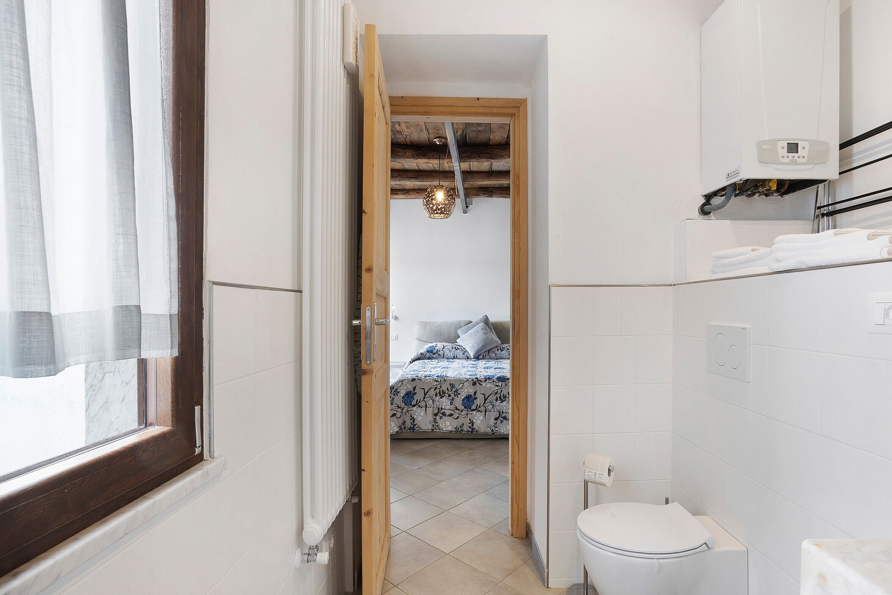 Ein Badezimmer mit Toilette, Dusche und einem Bett, das durch eine offene Tür sichtbar ist.