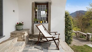 Eine Steintreppe führt zu einem Fenster mit Blumentöpfen, einem Holzstuhl und einer Stebrücke im Hintergrund.