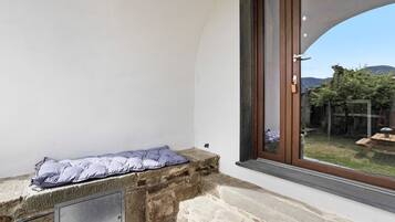 Un banco de piedra con cojín, una ventana con vistas a un jardín y una puerta con picaporte.