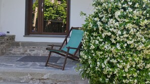 Eine Steintreppe führt zu einer Tür, davor steht ein grüner Stuhl, ein Blumentopf und ein Schild an der Wand.