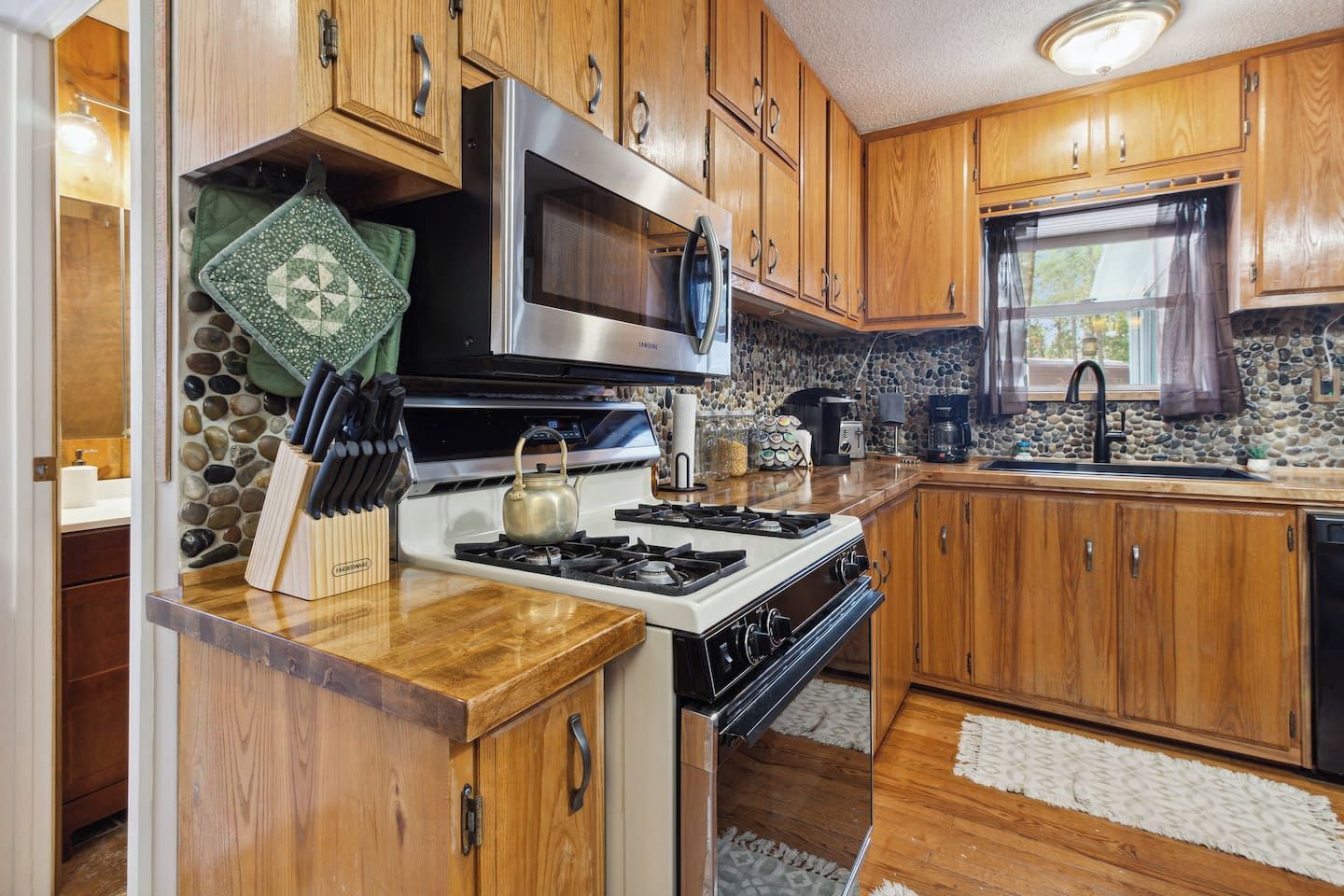 Una cocina con armarios de madera, estufa, microondas y protector de pared de piedra.
