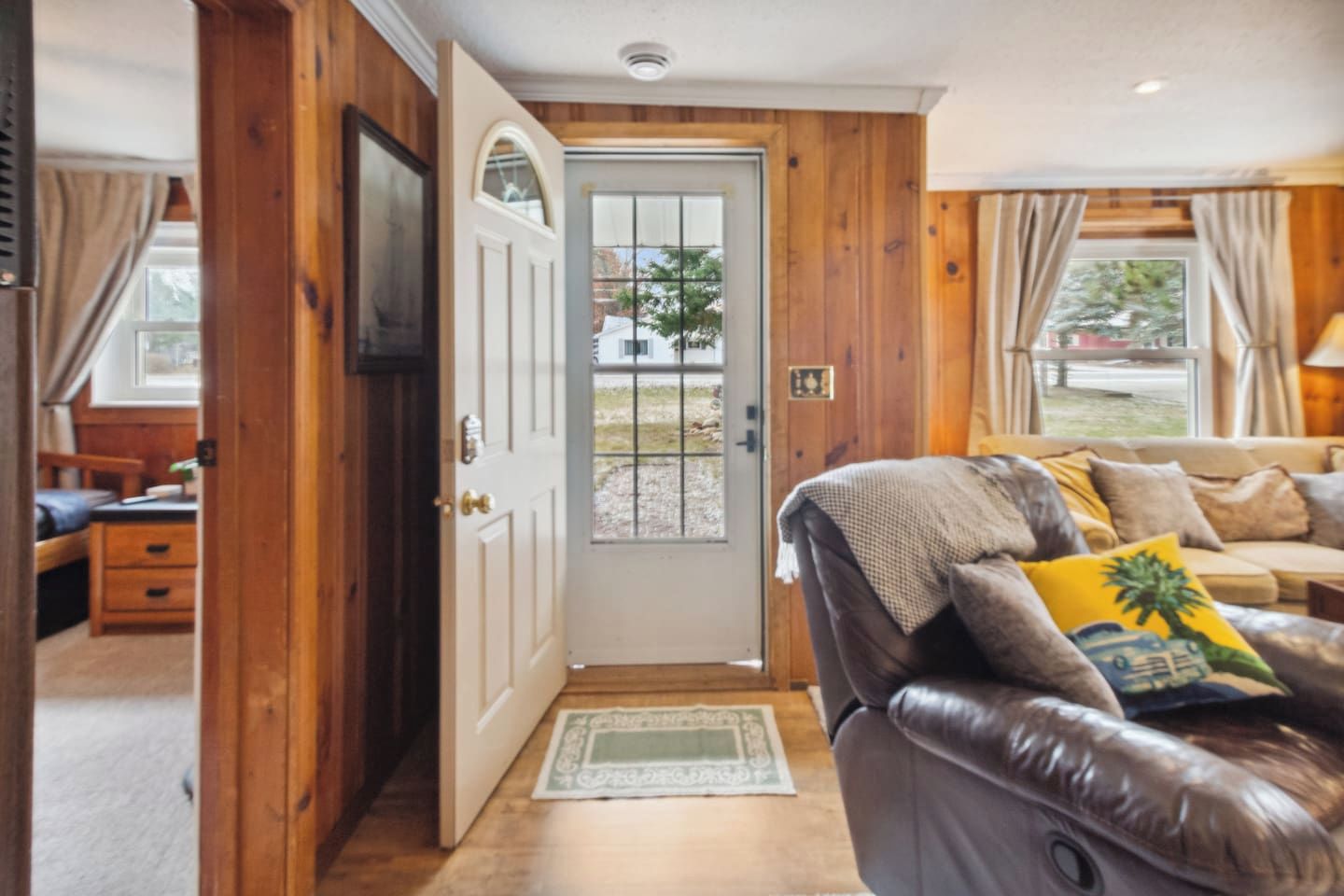 Un salon chaleureux avec un canapé en cuir, une porte en bois et une vue sur l’extérieur.