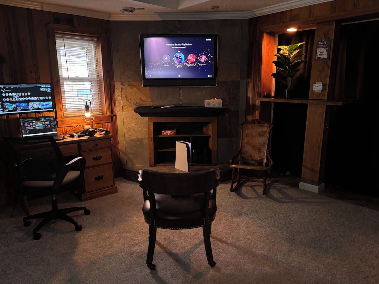 Une pièce comprenant un bureau, un ordinateur, une chaise et un téléviseur diffusant un jeu vidéo.